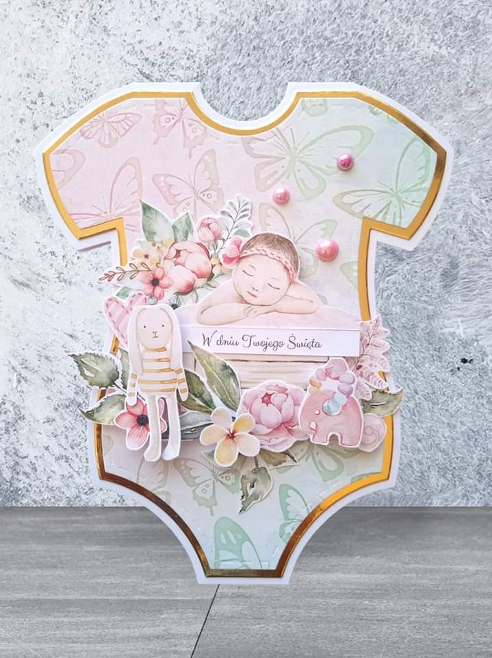 Ręcznie robiona kartka okolicznościowa w kształcie dziecięcego body, zdobiona motywami kwiatowymi, motylami, figurką śpiącego dziecka, królika i słonia, z napisem 'W dniu Twojego Święta'.