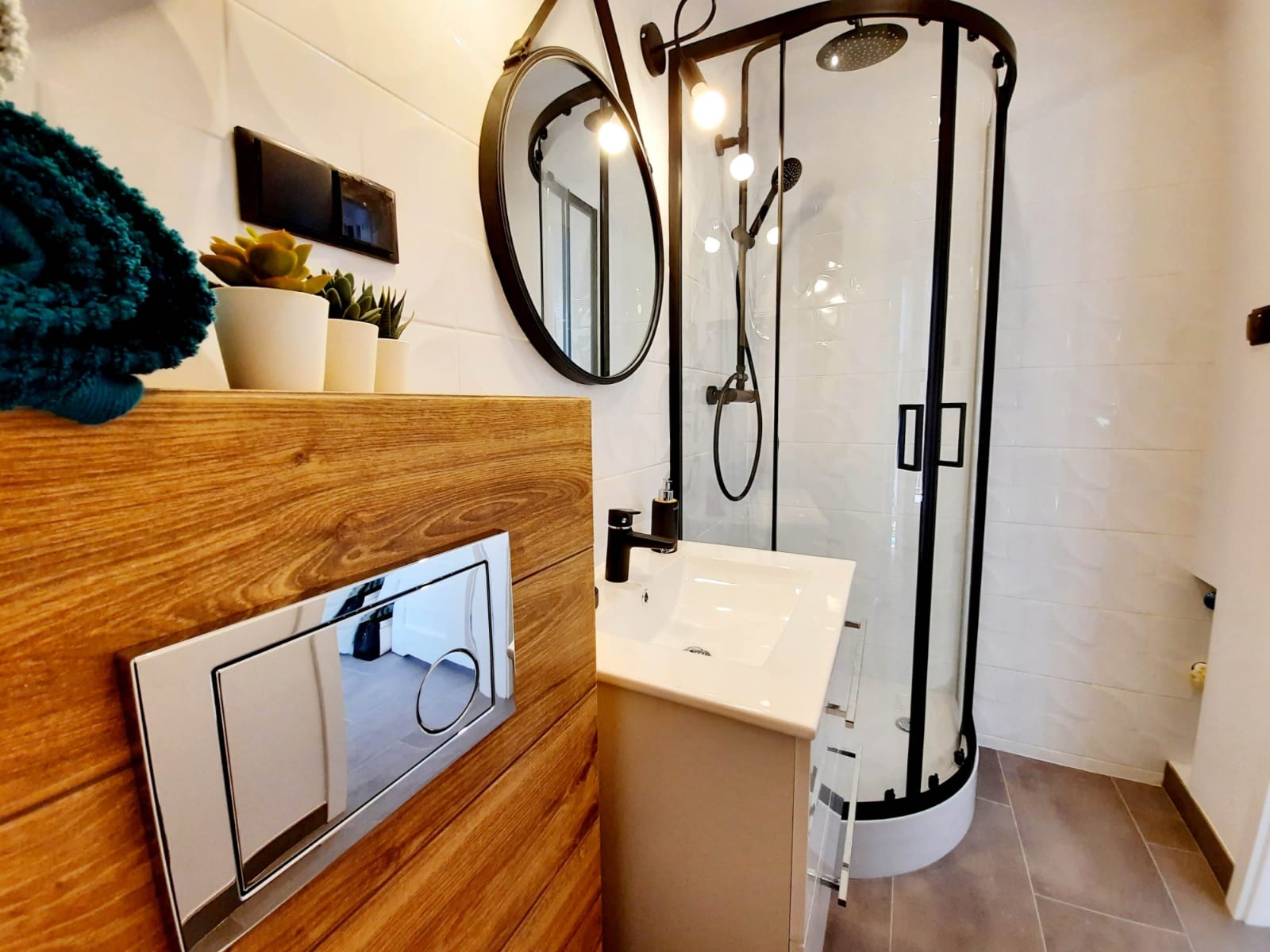 Nowoczesna łazienka w Oświęcimiu z kabiną prysznicową z czarnymi ramami, okrągłym lustrem na pasku i drewnianą obudową toalety z chromowanym przyciskiem spłukującym, uzupełniona o białą umywalkę...