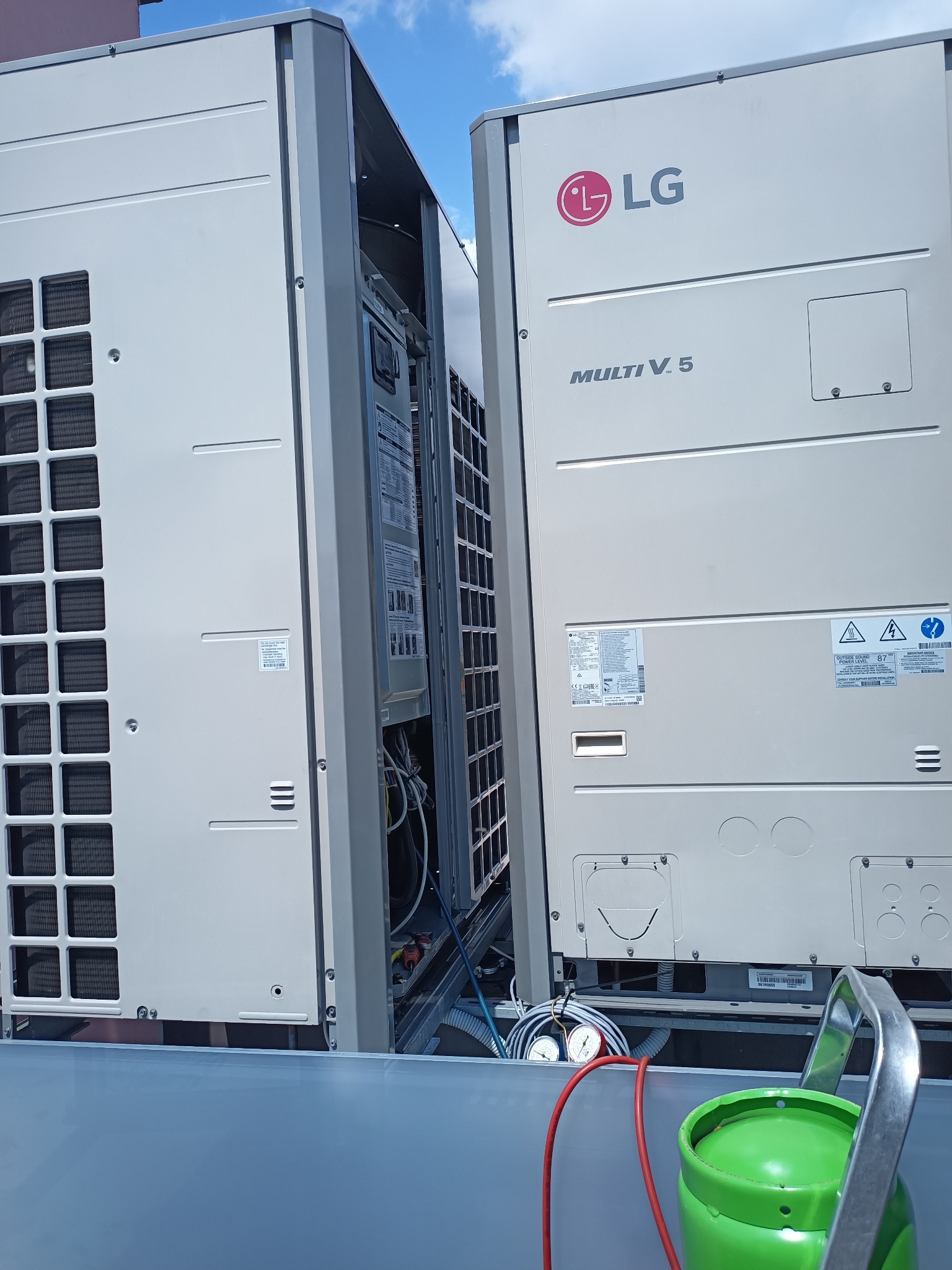 Dwa moduły klimatyzacji LG Multi V 5 na dachu, widoczne manometry i butla z czynnikiem chłodniczym, sugerujące serwis lub instalację.
