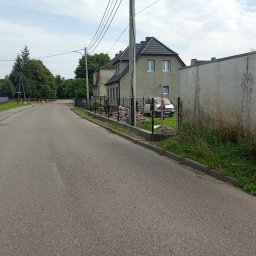 Lakiernia Proszkowa Kewin Radowski - Montaż ogrodzenia panelowego przy drodze; widoczne słupki i panele, w tle dom i zaparkowany samochód. Prace w toku, przygotowanie podłoża.
