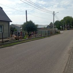 Lakiernia Proszkowa Kewin Radowski - Montaż ogrodzenia panelowego na posesji w trakcie realizacji. Widoczne panele, słupki i ekipa montażowa przy pracy. Elementy ogrodzenia składowane obok.