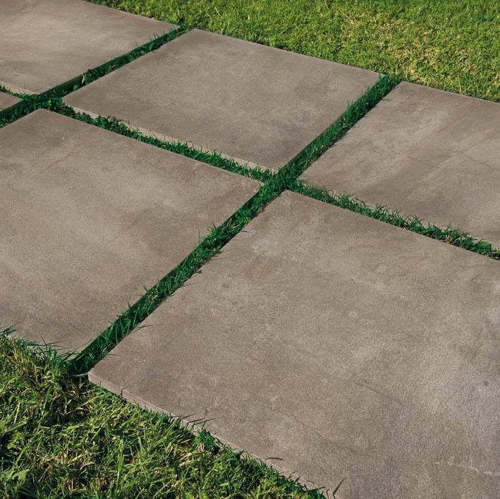 Szare, kwadratowe płyty chodnikowe ułożone w trawie, tworzące ścieżkę ogrodową.