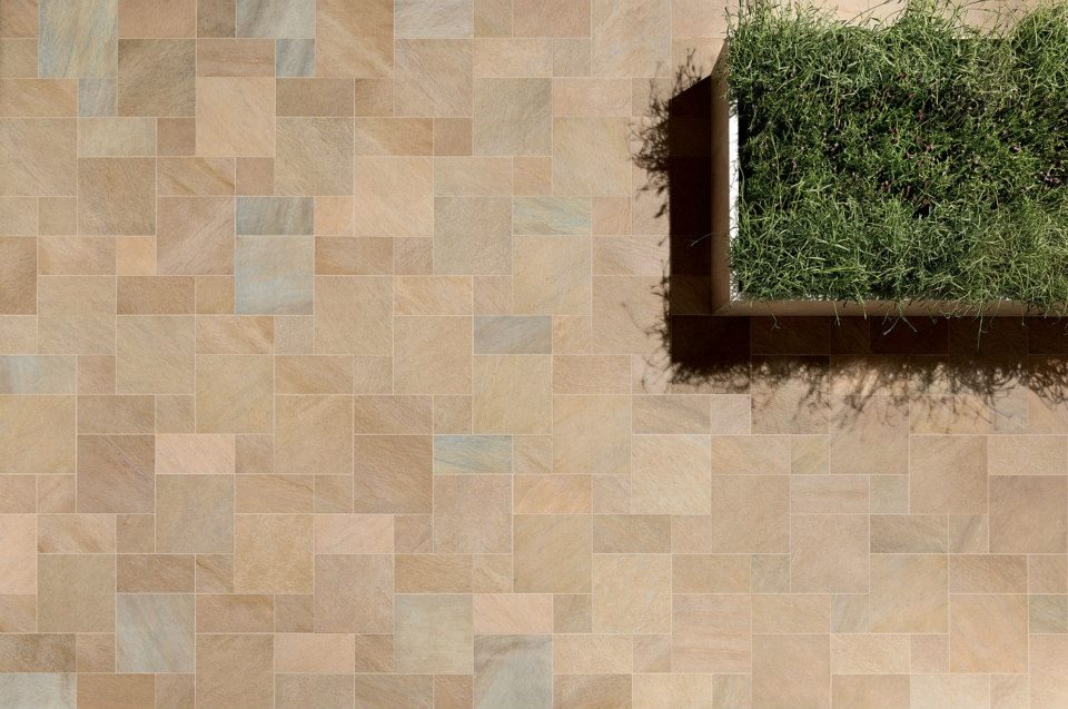 Ułożona zróżnicowana kompozycja z płytek tarasowych w odcieniach beżu i brązu, z donicą z zieloną trawą w prawym górnym rogu, widok z góry.