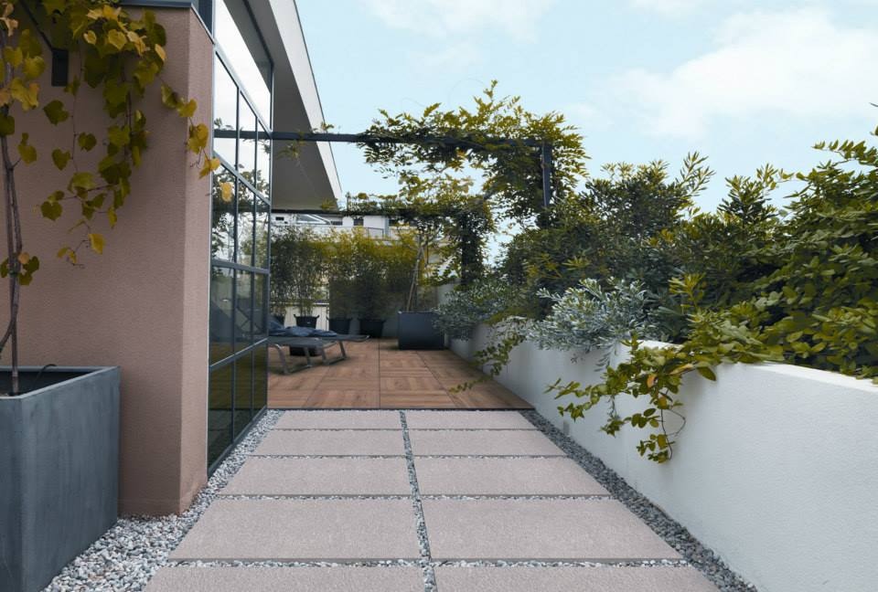 Ułożone płyty tarasowe w Poznaniu z drobnym żwirem między nimi, prowadzące do drewnianego tarasu z zielenią w tle.