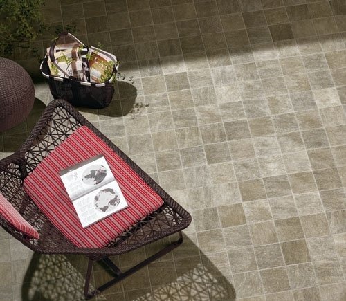 Szare płytki podłogowe na zewnątrz, z wiklinowym krzesłem z czerwoną poduszką i otwartą książką oraz koszem piknikowym w rogu.