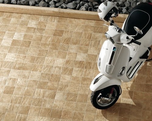 Beżowa, kwadratowa podłoga z płytek ceramicznych na zewnątrz budynku, z zaparkowanym białym skuterem i kaskiem