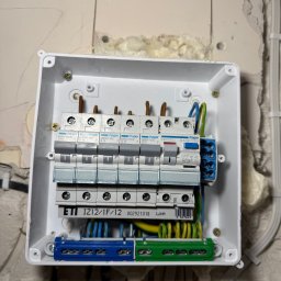 Sebastiansak - Otwarta skrzynka elektryczna z zamontowanymi bezpiecznikami Hager MBN116E, zabezpieczeniem różnicowoprądowym Hager CDC225J i listwami zaciskowymi ETI IZ12/1F/12, widoczne kable w kolorach...