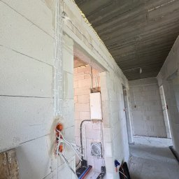 Sebastiansak - Wewnętrzne instalacje elektryczne w surowym stanie budynku z białego betonu komórkowego, widoczne kable w peszlach i puszki podtynkowe, skrzynka elektryczna na ścianie, narzędzia w czarnej skrzynce...