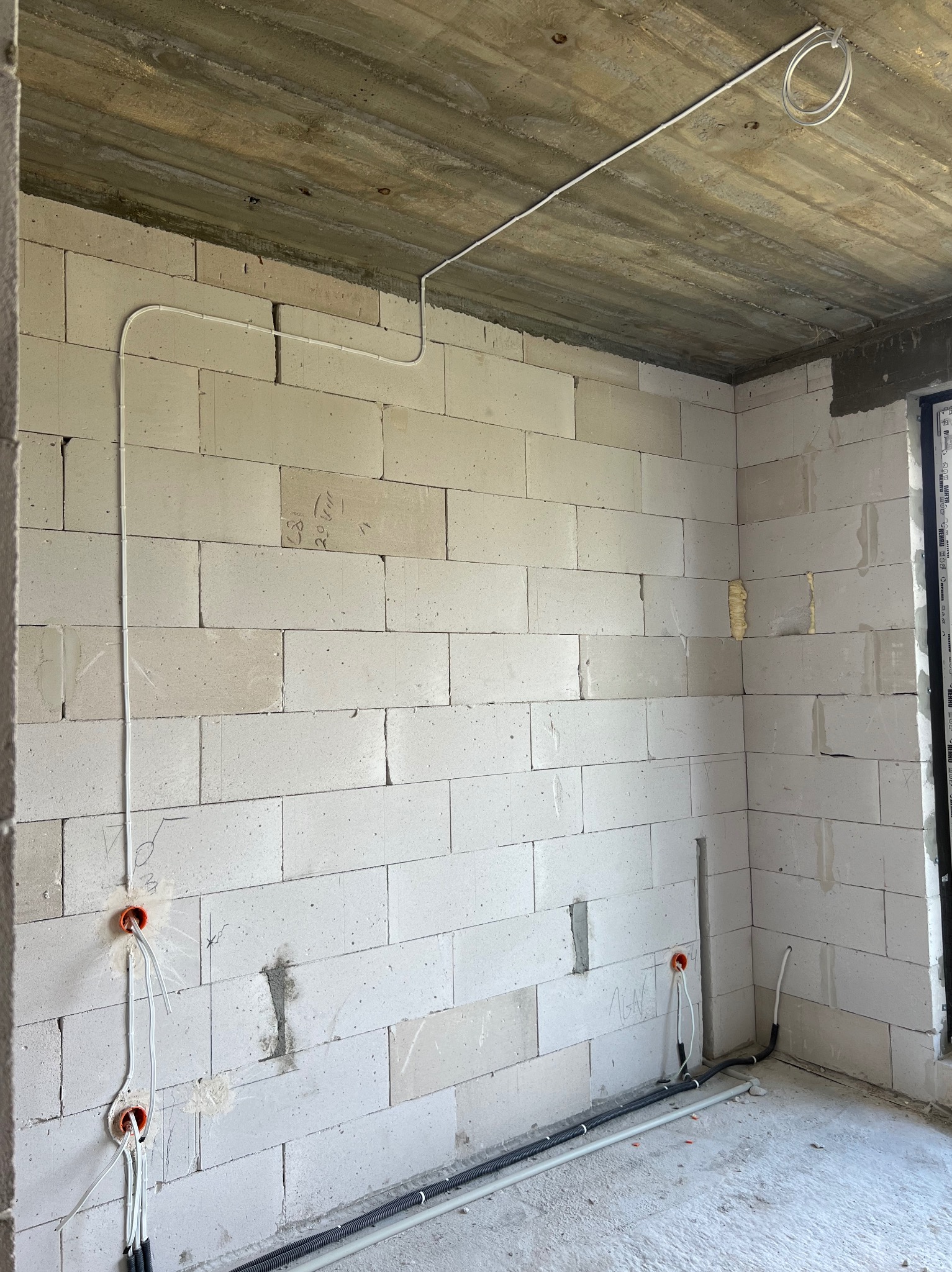 Surowy stan wnętrza w Siedlcach z widocznymi przewodami elektrycznymi poprowadzonymi po ścianach z betonu komórkowego i pod sufitem, przygotowanymi do dalszych prac wykończeniowych.