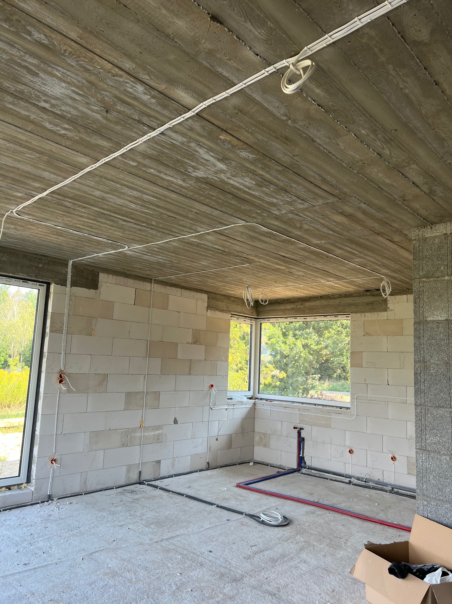 Surowy stan wnętrza z widocznymi przewodami elektrycznymi ułożonymi na suficie i ścianach, okablowanie w listwach, instalacja wodna z rurami w kolorach niebieskim i czerwonym, ściany z białych...