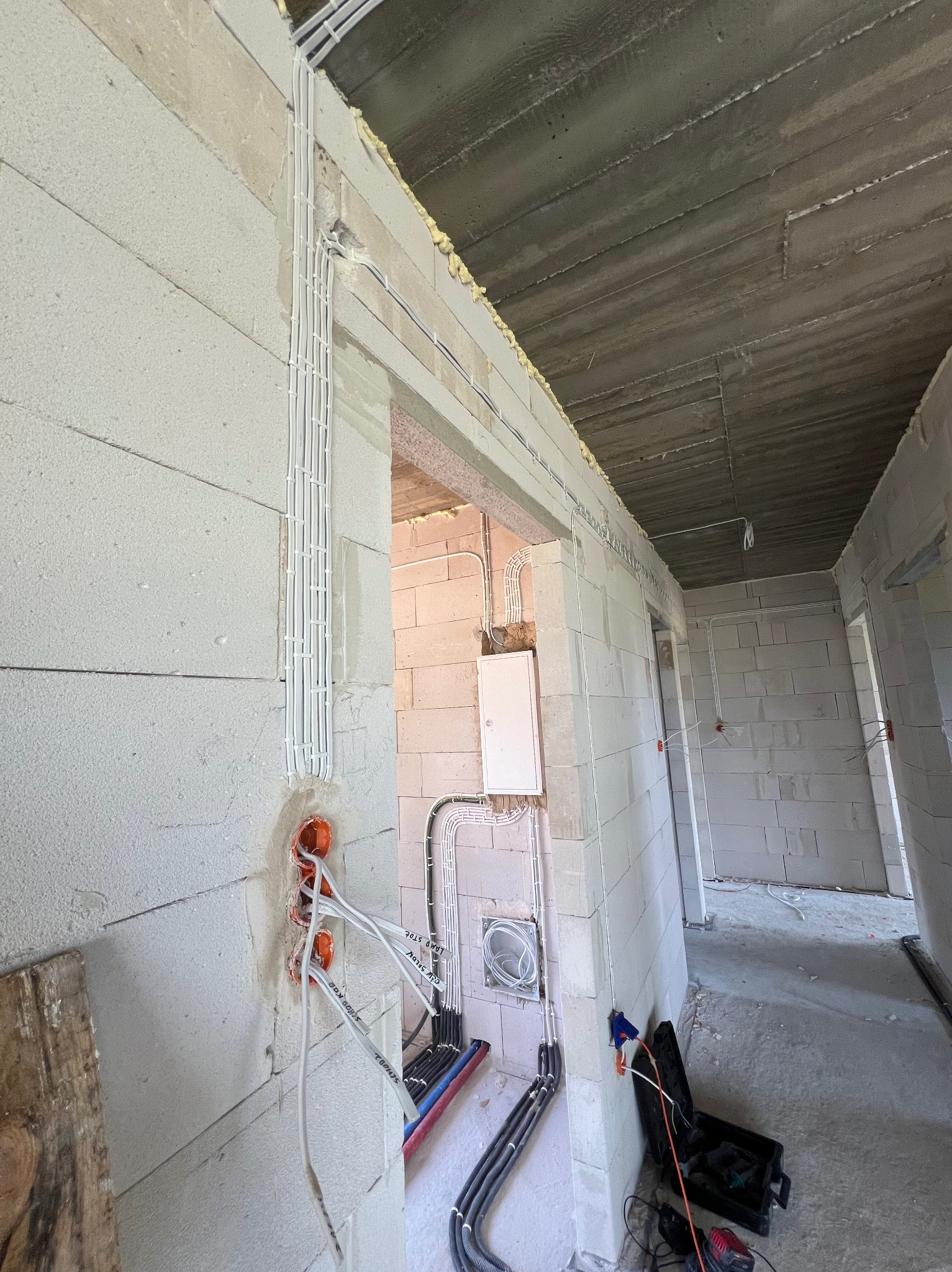 Wewnętrzne instalacje elektryczne w surowym stanie budynku z białego betonu komórkowego, widoczne kable w peszlach i puszki podtynkowe, skrzynka elektryczna na ścianie, narzędzia w czarnej skrzynce...