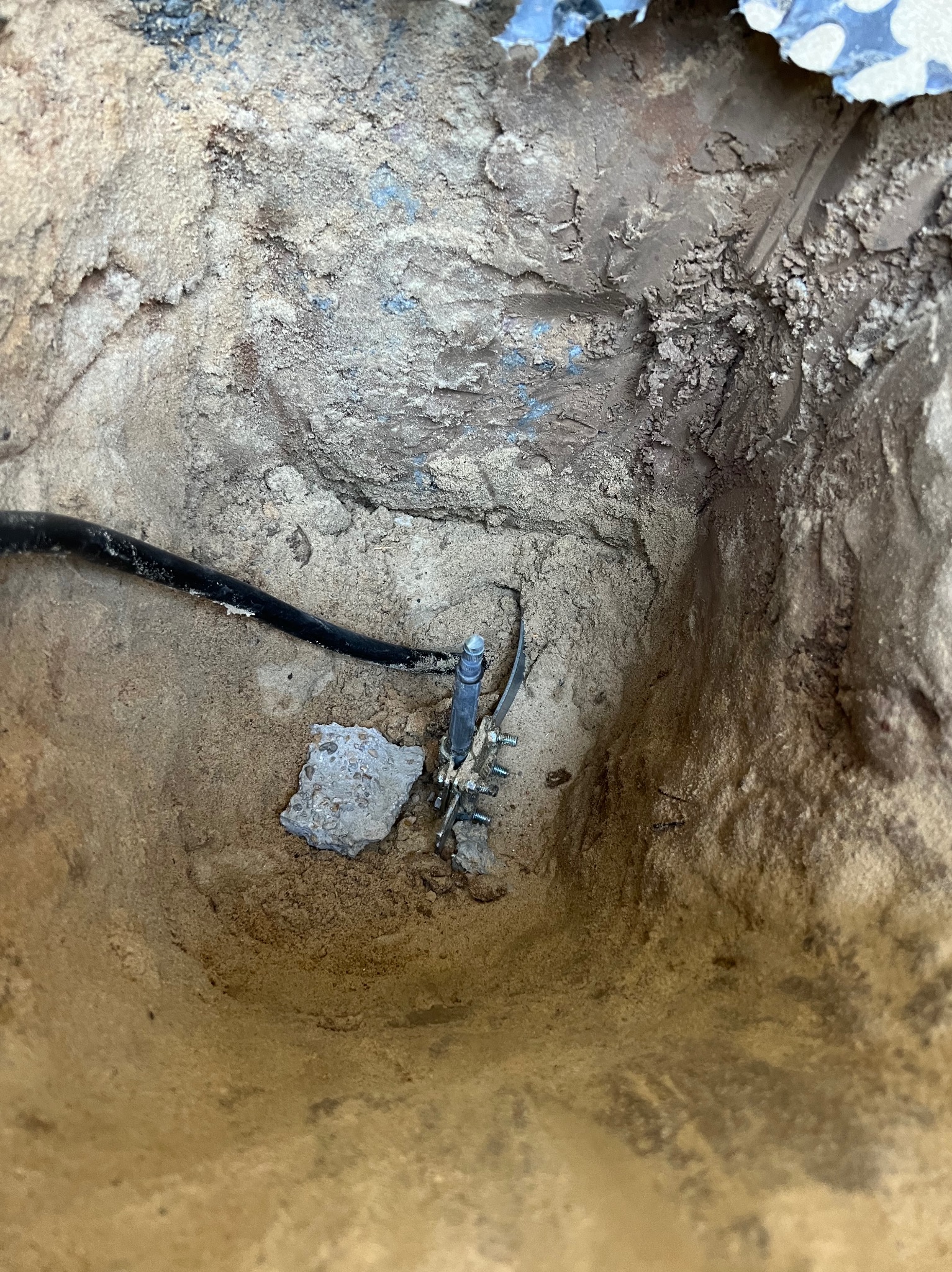 Uziemienie w wykopie wypełnionym piaskiem; widoczny przewód uziemiający i złącze z metalową szpilką wbite w ziemię.