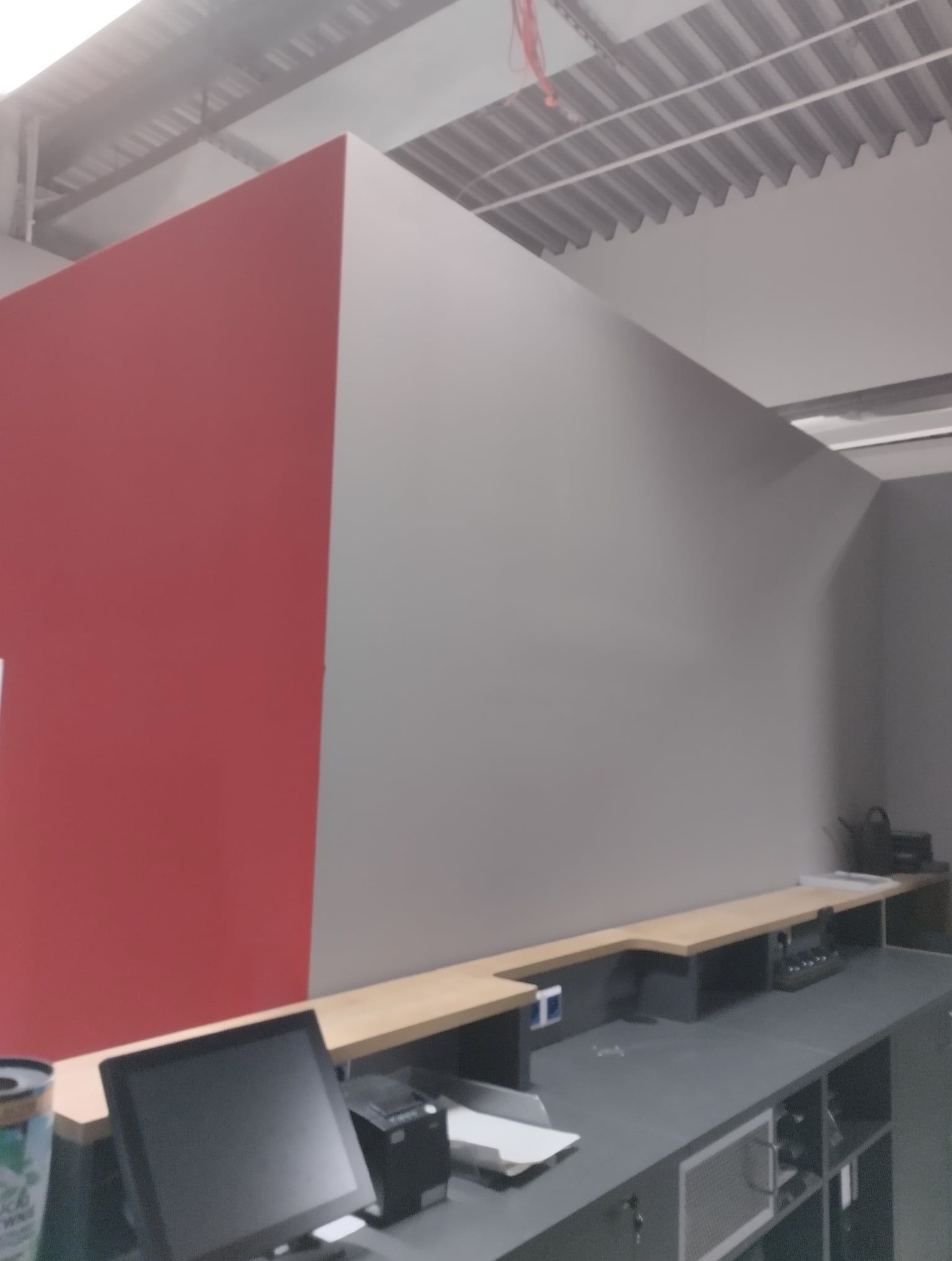 Świeżo pomalowane, dwukolorowe ściany w biurze, widok zza biurka z monitorem i drukarką, sufit z blachy trapezowej.