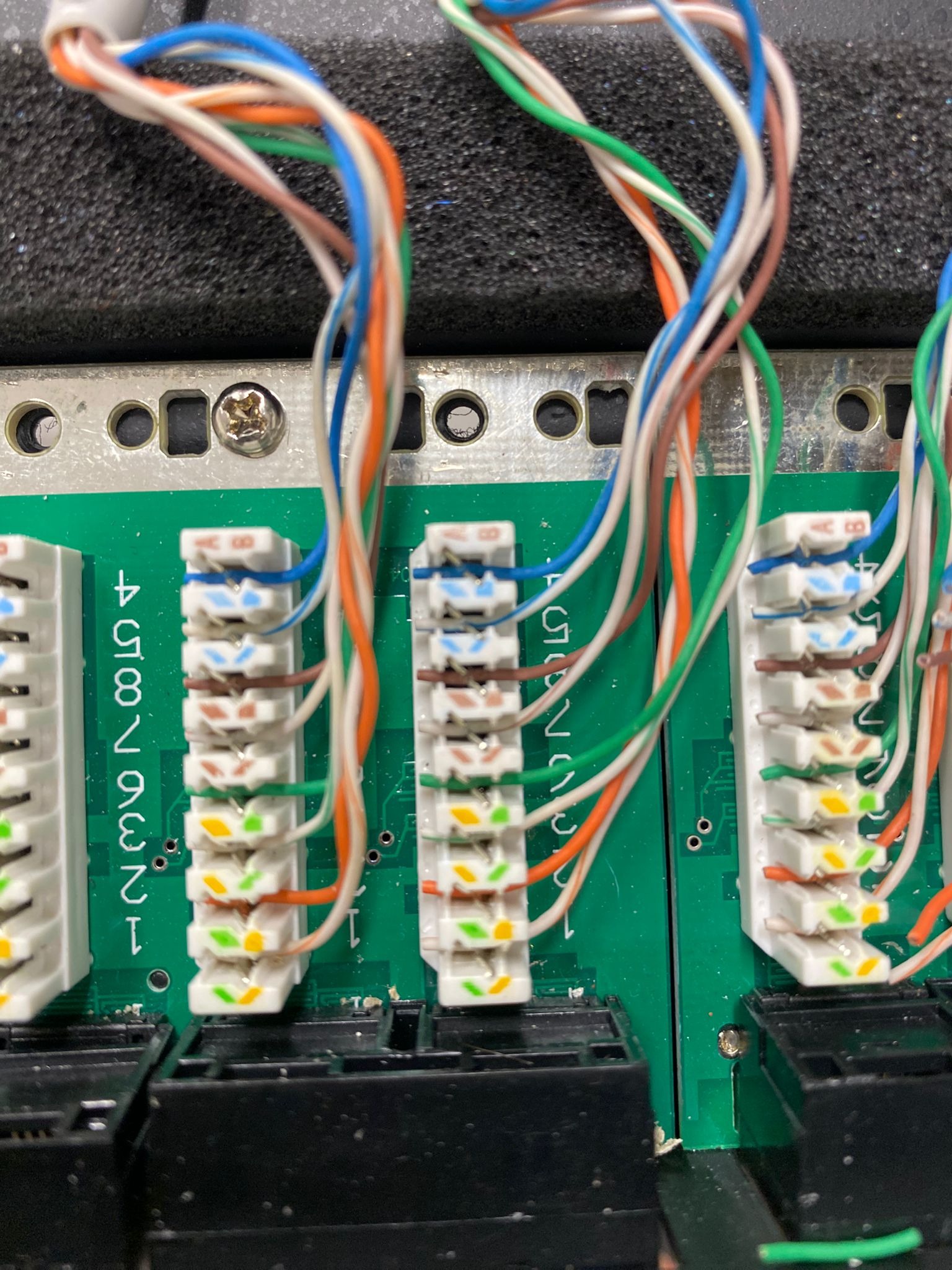 Szczegółowe ujęcie panelu krosowniczego z podłączonymi kablami ethernet o różnych kolorach (niebieski, pomarańczowy, zielony, brązowy, biały) na zielonej płytce drukowanej z numeracją portów.