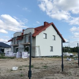 Perfekt Dach Kamil Jurczak - Nowy dom w trakcie budowy z czerwoną dachówką, widoczne rusztowania i materiały izolacyjne na placu budowy w słoneczny dzień.