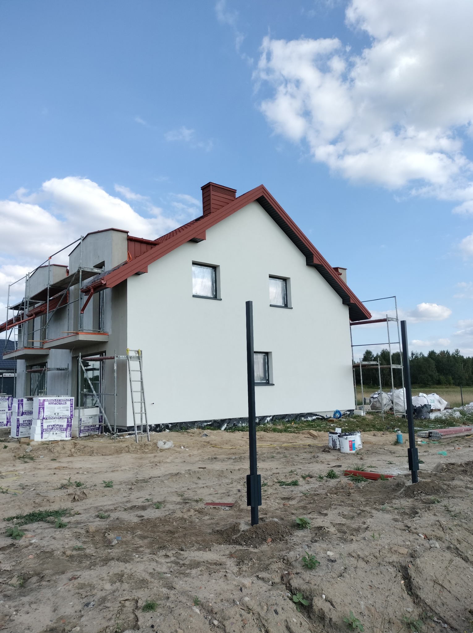 Wymiana dachu z czerwonej blachy na nowym domu w Jednorożcu, widoczne rusztowania i materiały budowlane na placu budowy.