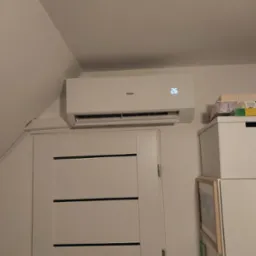 Biały klimatyzator Haier z wyświetlaczem temperatury 26 stopni Celsjusza zamontowany nad białą, nowoczesną drzwiami w pokoju na poddaszu.