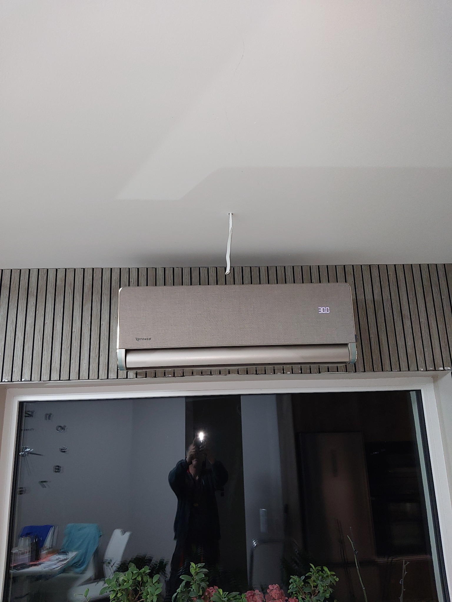 Zamontowany klimatyzator Rotenso w mieszkaniu w Gryfinie, widoczny na tle ściany z drewnianymi panelami, odbicie fotografa w szybie okna.