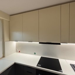 Stolarz Łukasz Kołodziejczyk - Beżowe szafki kuchenne podświetlone listwą LED, czarny blat z płytą indukcyjną, widoczne gniazdko elektryczne i niedokończone podłączenie kabla.