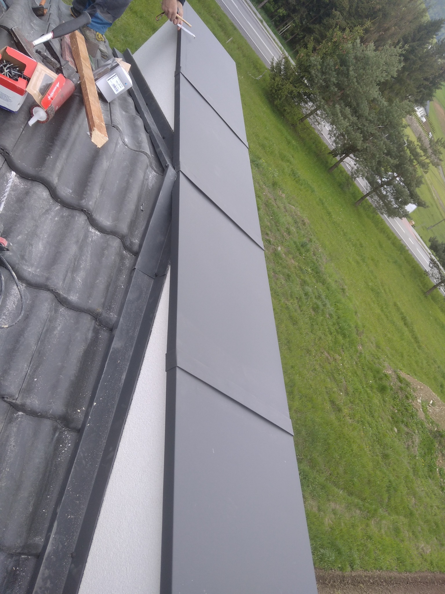 Montaż paneli na dachu z widoczną izolacją, narzędziami i fragmentem krajobrazu w tle.