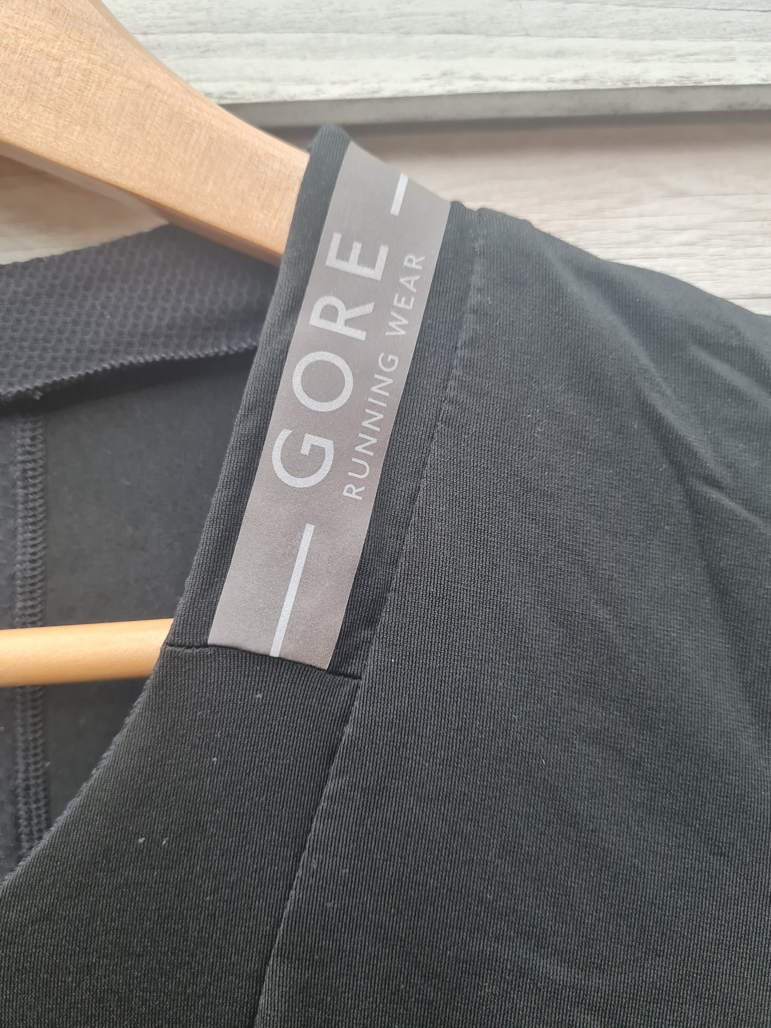 Czarne sportowe ubranie z widocznym logo GORE RUNNING WEAR na wieszaku, ukazujące strukturę materiału.