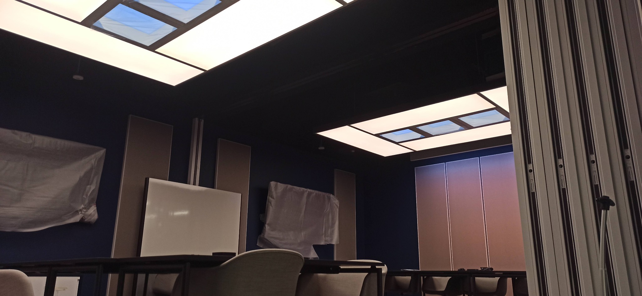 Nowoczesne oświetlenie sufitowe z panelami LED w pomieszczeniu biurowym z niebieskimi ścianami i akustycznymi panelami ściennymi.