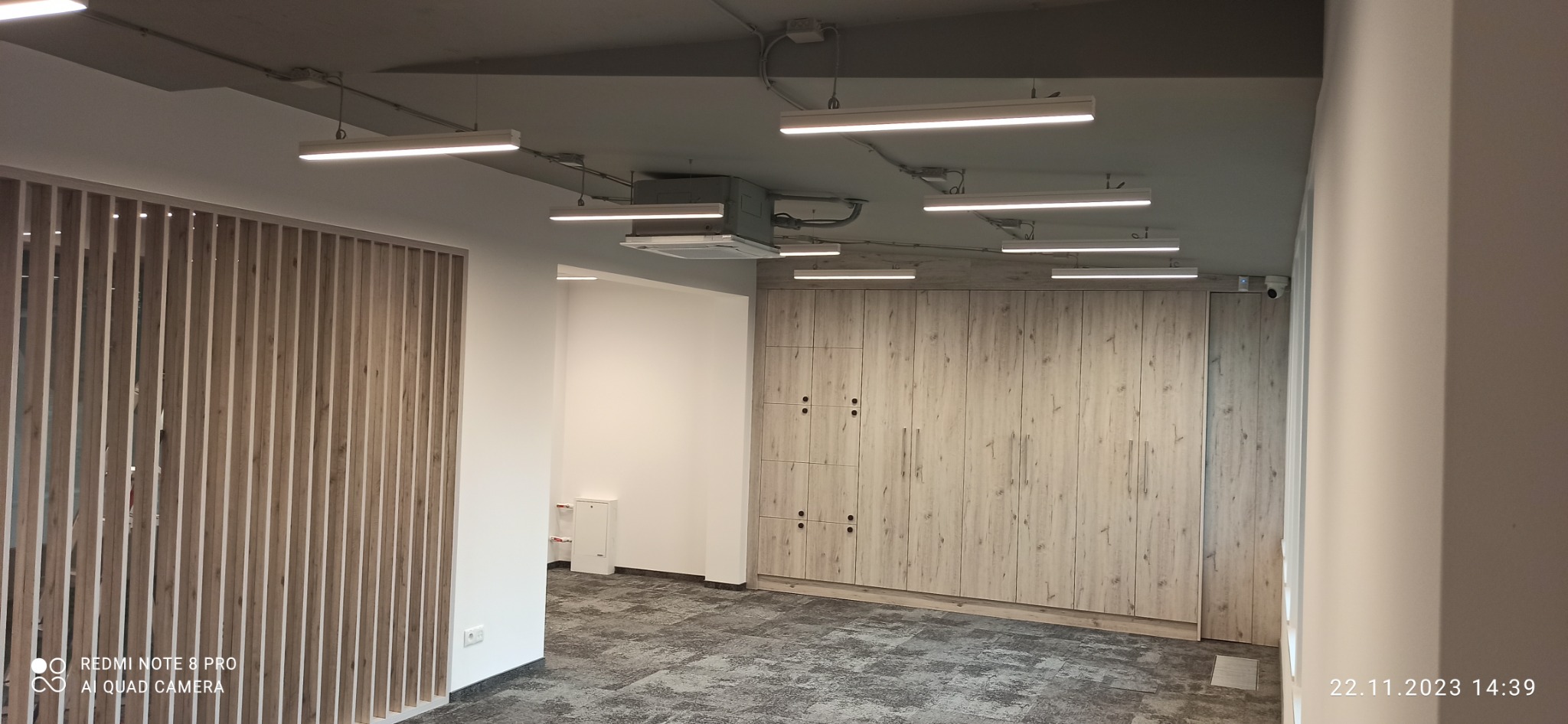 Wnętrze biurowe z zamontowanym oświetleniem LED, drewnianą ścianką działową i szafą w zabudowie z jasnego drewna.