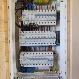 Rozdzielnica elektryczna Hager z zainstalowanymi bezpiecznikami i przewodami w obudowie zamontowanej na drewnianej ścianie.