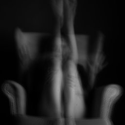 Zuzanna Kulesa - Czarno-białe, rozmyte zdjęcie kobiety siedzącej na fotelu z uniesionymi nogami, twarz zasłonięta dłońmi, artystyczny nieostry efekt.