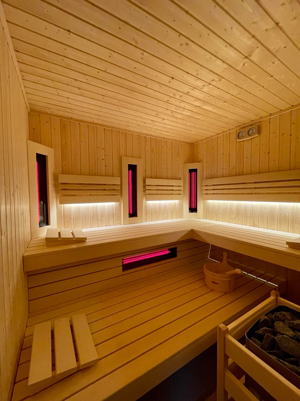 Wnętrze drewnianej kabiny z podświetlanymi panelami infrared, wiadro i kamienie do sauny w rogu.