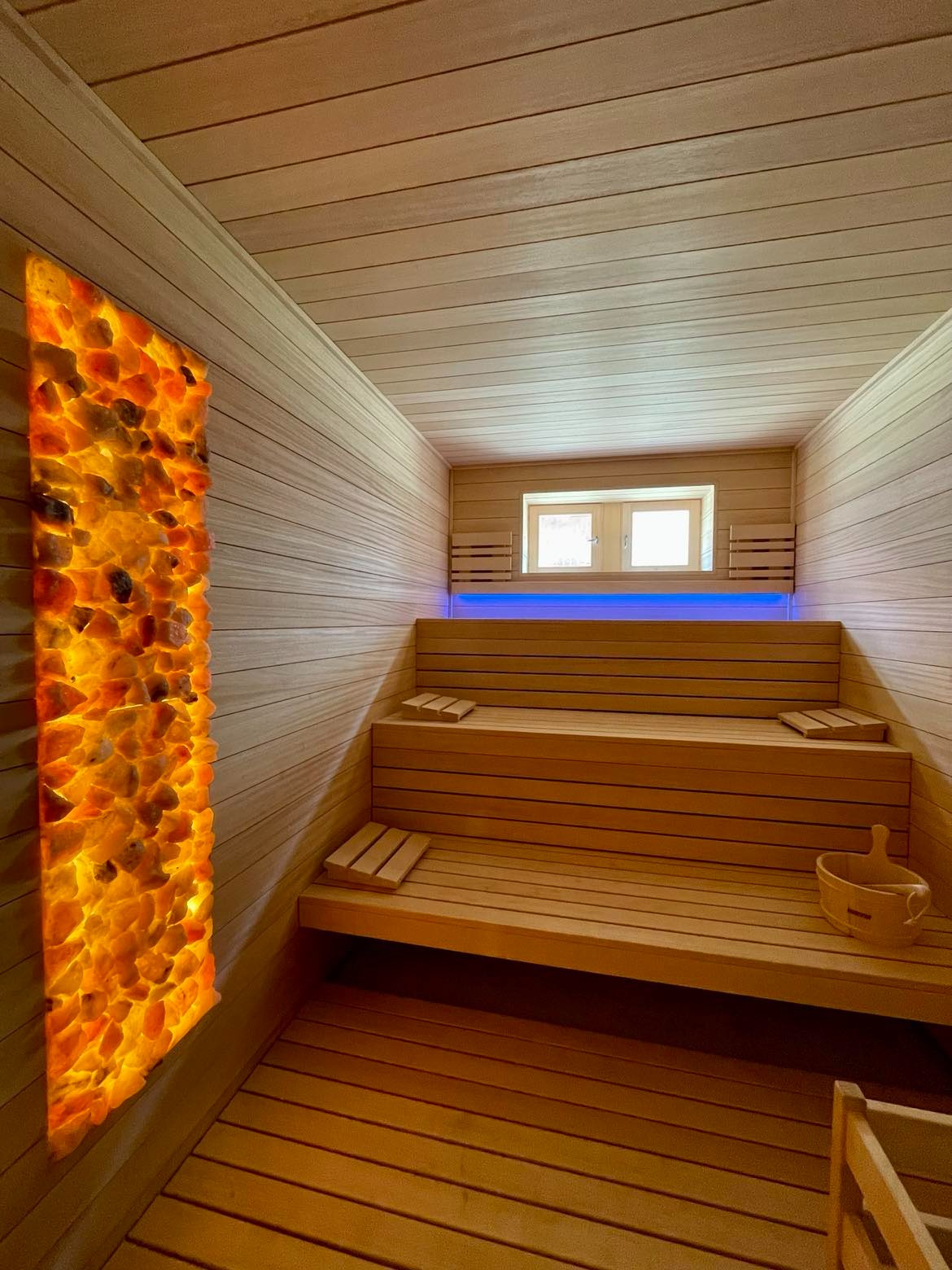 Drewniana sauna z podświetlaną ścianą z kamieni solnych w Warszawie, widoczne ławy i drewniane wiaderko.
