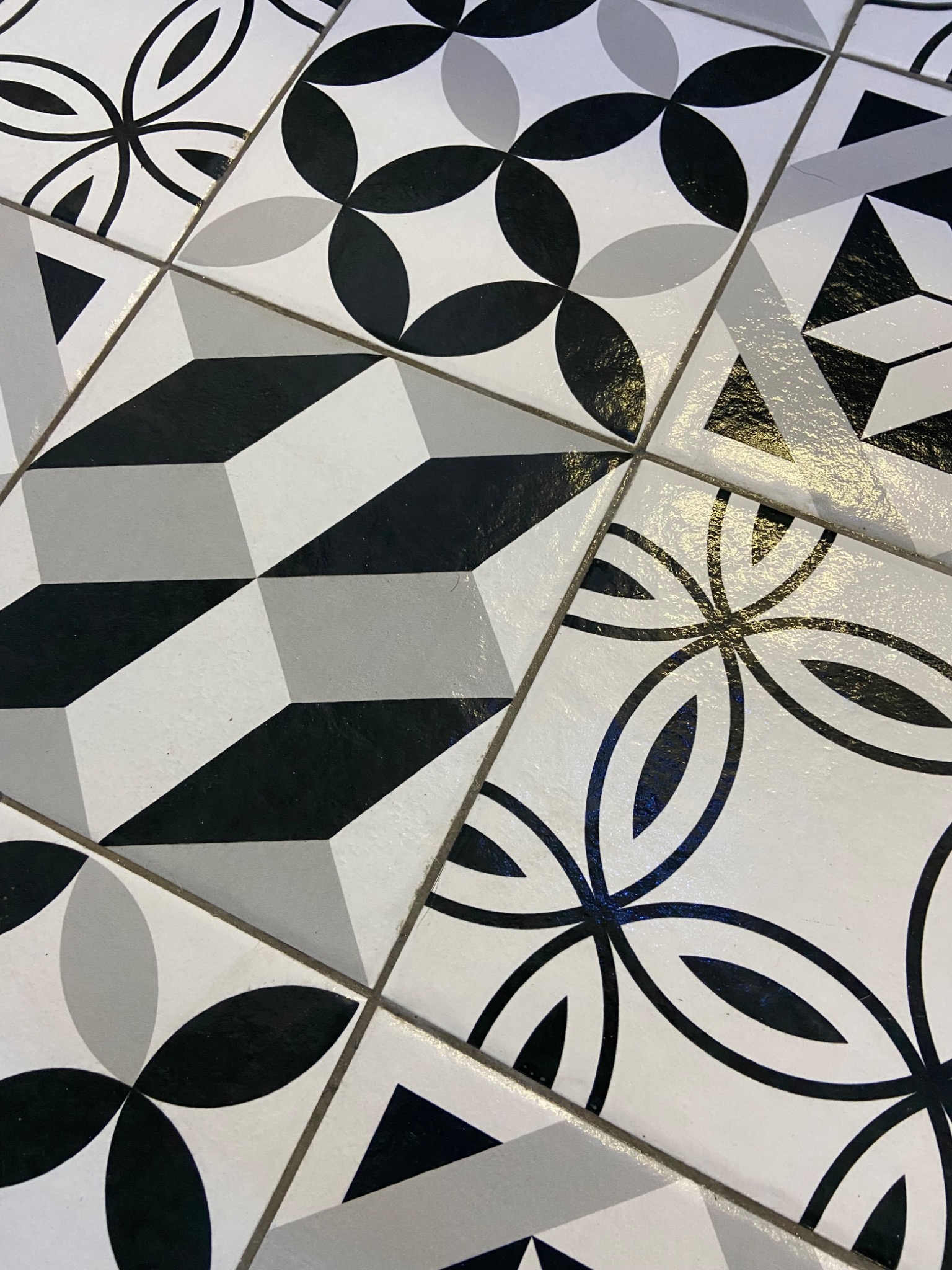 Wzorzyste, czarno-białe płytki podłogowe ułożone w geometryczne i kwiatowe motywy, z widocznymi fugami.