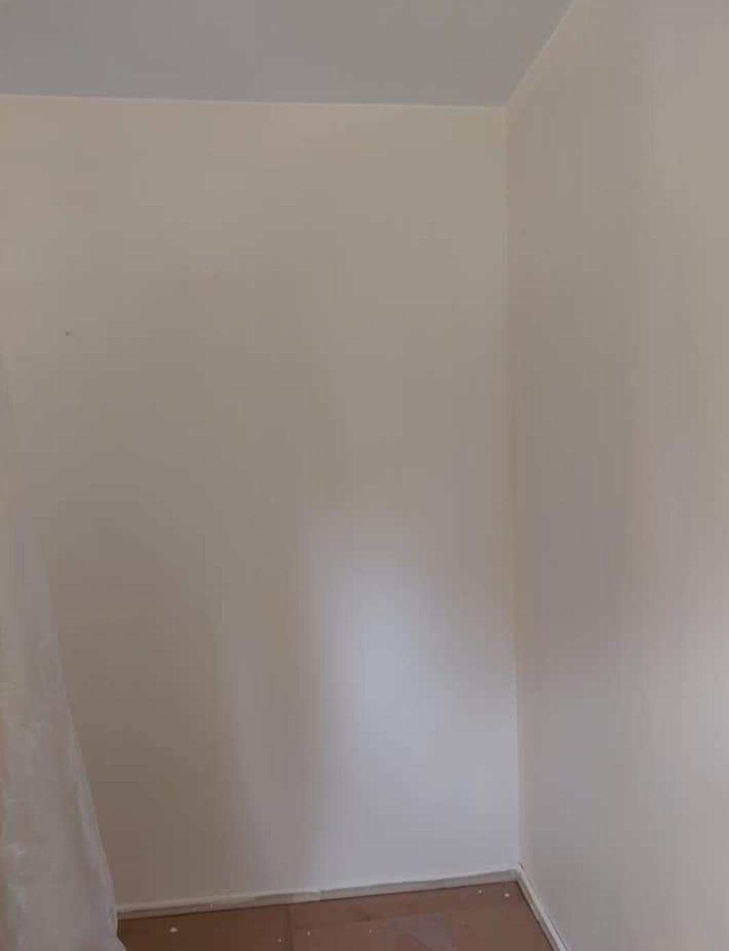 Świeżo pomalowany róg pokoju z beżowymi ścianami i brązową podłogą, widoczne drobne niedoskonałości malowania przy podłodze.