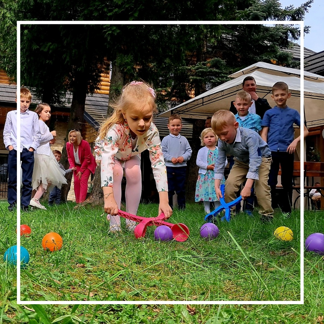 Dzieci grają w grę z kolorowymi piłkami i plastikowymi szczypcami na trawie podczas imprezy plenerowej.
