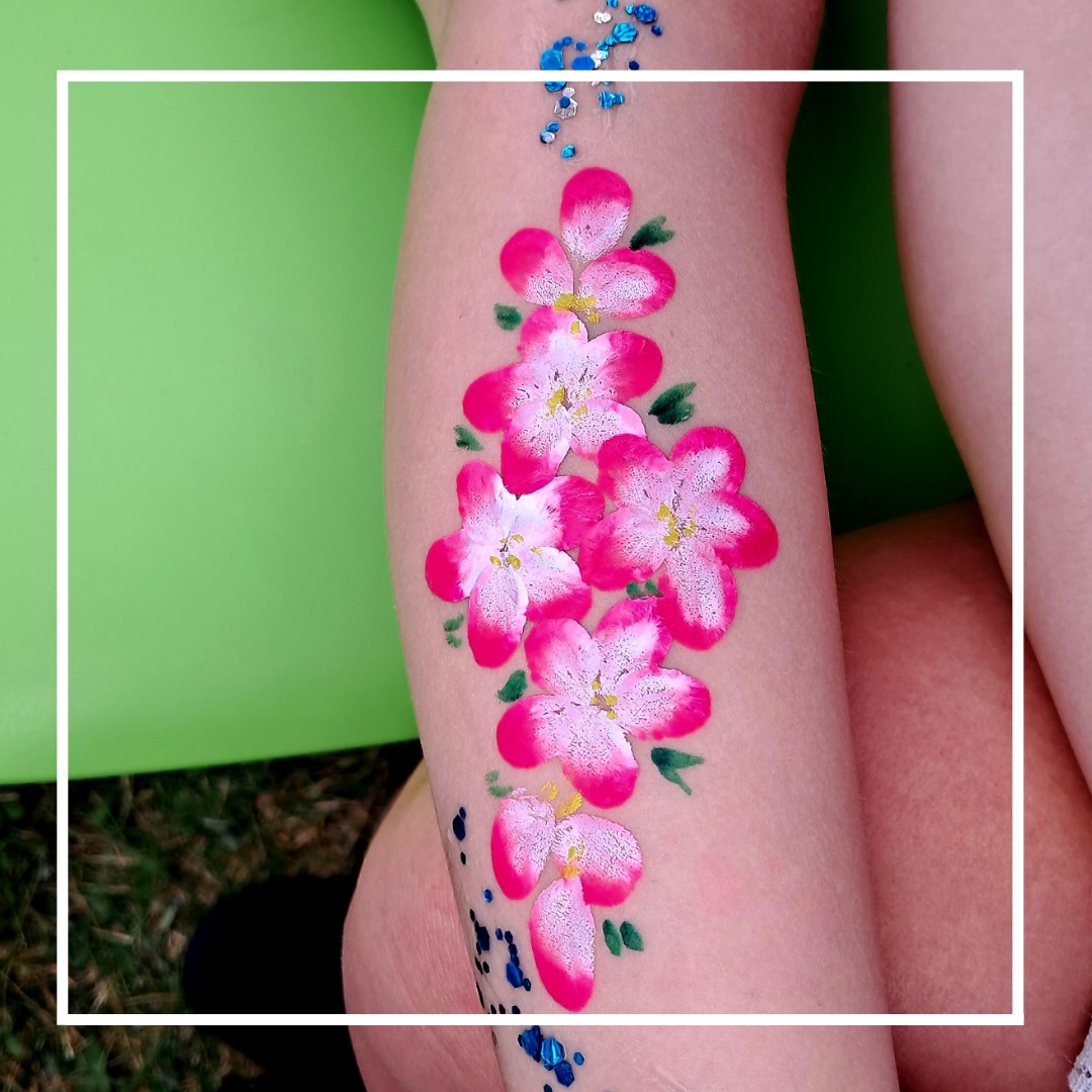 Ręcznie malowane różowe kwiaty wiśni z brokatem na nodze dziecka, zielone tło.