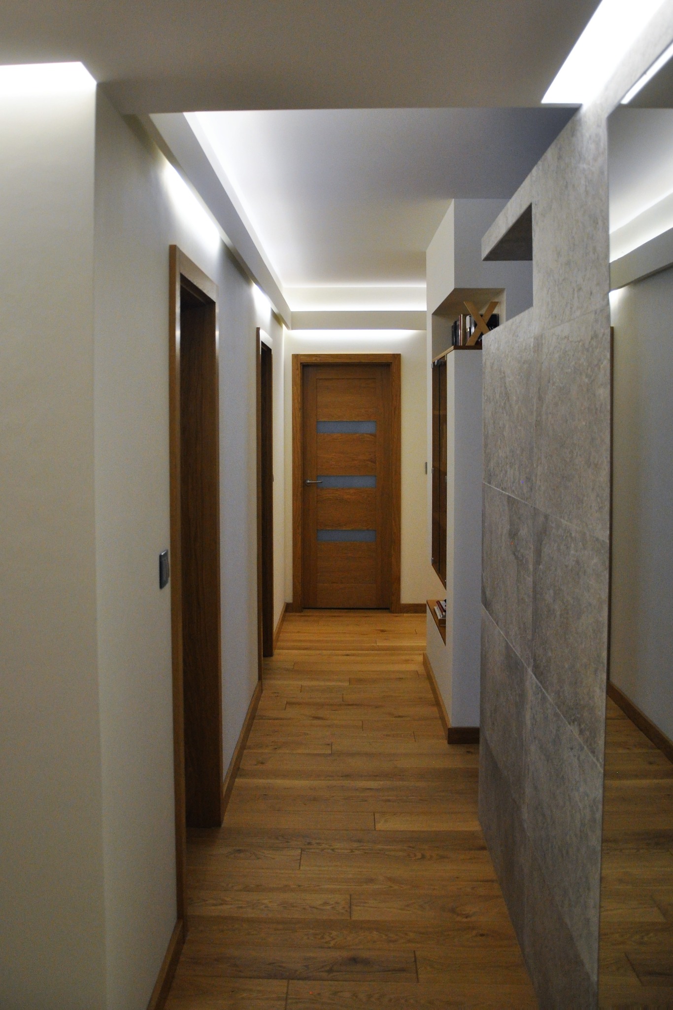 Korytarz w mieszkaniu z drewnianą podłogą, drzwiami z przeszkleniami i oświetleniem LED w suficie podwieszanym.