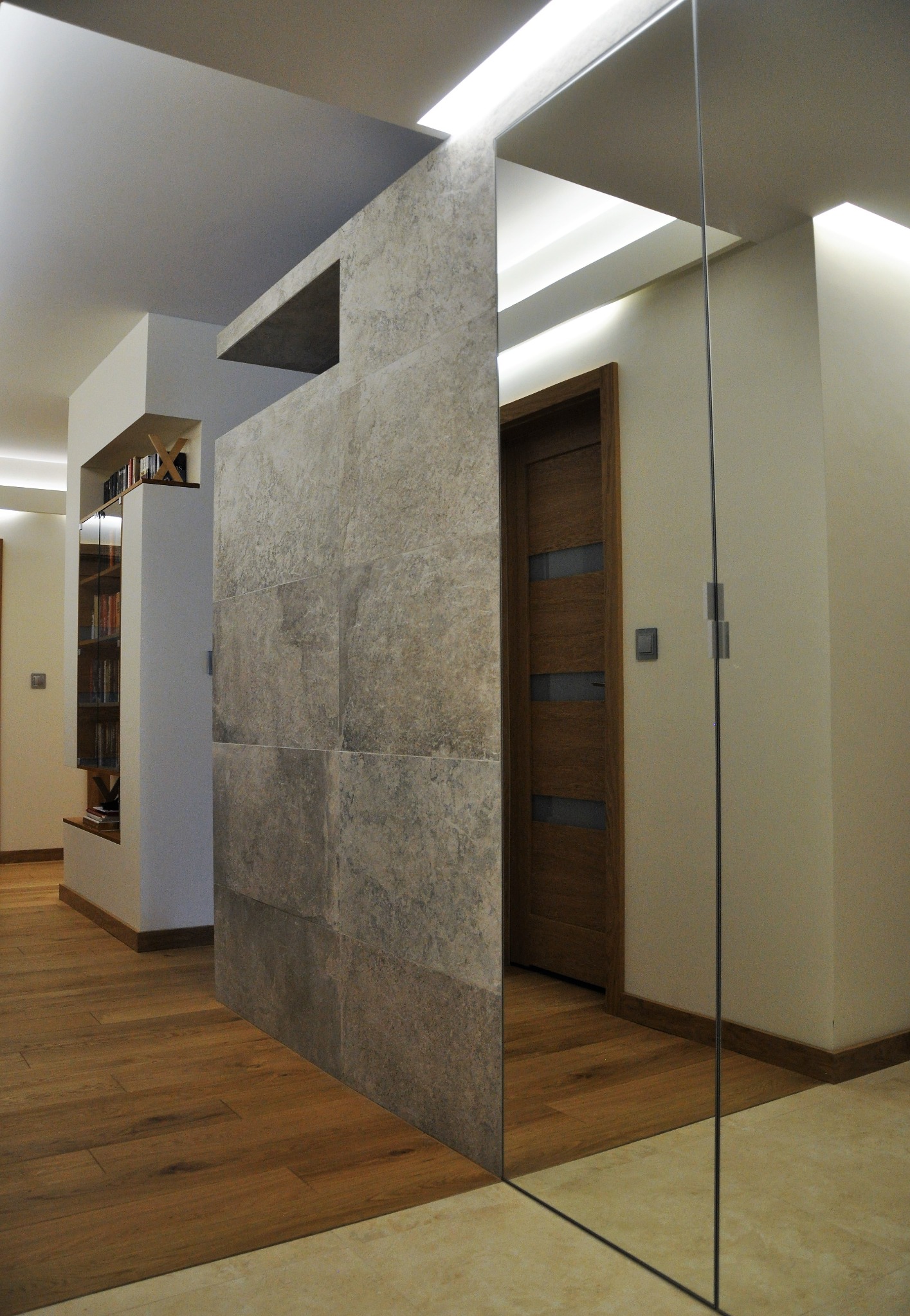 Nowoczesne wnętrze z płytami kamiennymi na ścianie, drewnianą podłogą i szklaną ścianą działową, oświetlenie LED w suficie.