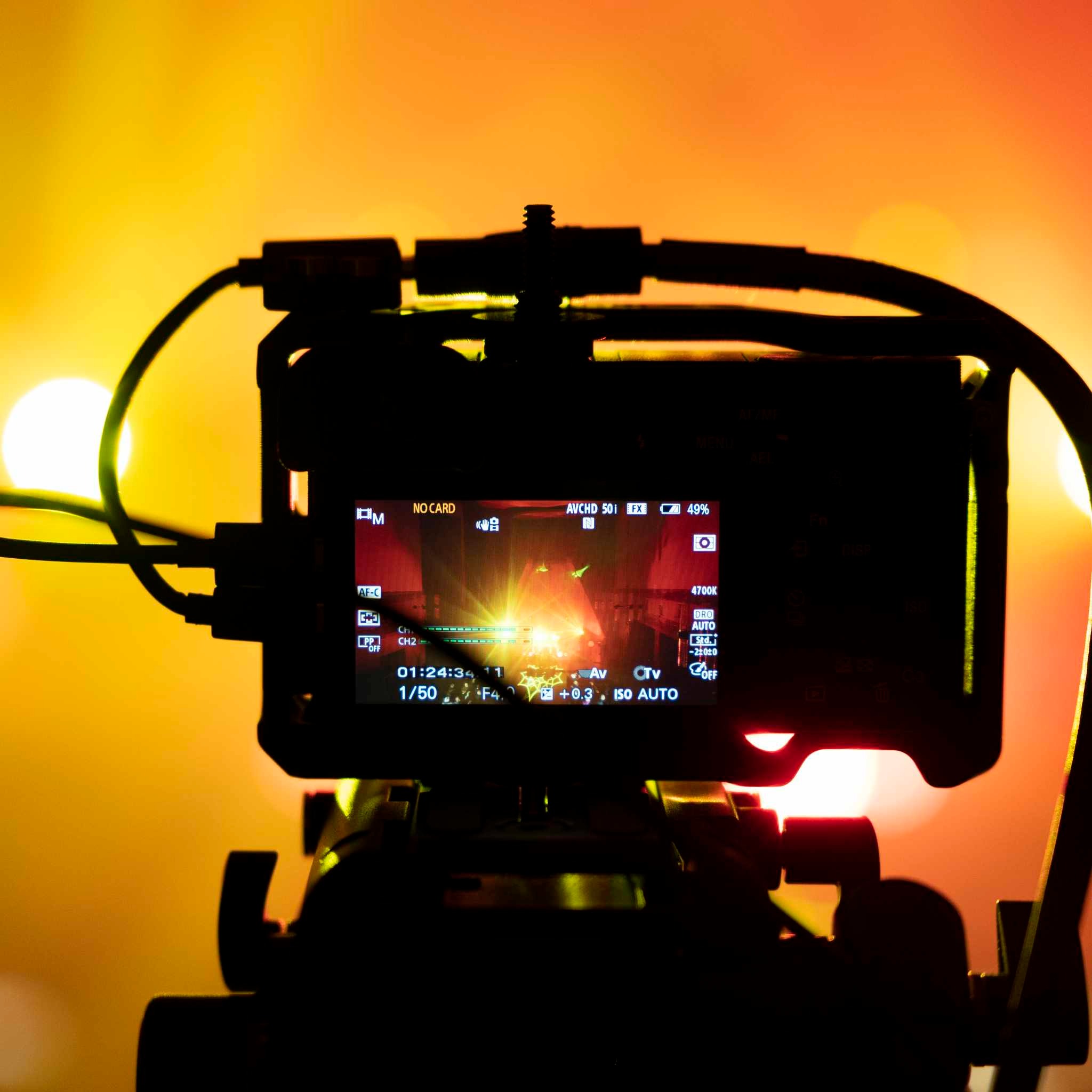 Profesjonalna kamera w trakcie nagrywania, widoczny ekran z ustawieniami ekspozycji i podglądem sceny w pomarańczowo-żółtym oświetleniu.