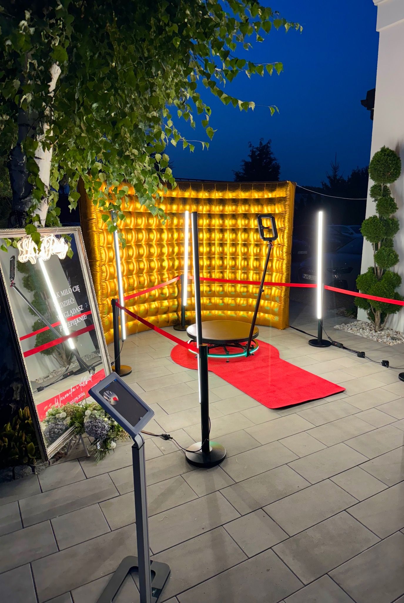 Złota, dmuchana ścianka z oświetleniem LED i czerwonym dywanem na zewnątrz, przygotowana do obsługi gości na imprezie.
