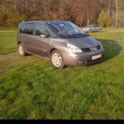 Brązowy minivan Renault Espace zaparkowany na trawiastym terenie z drzewami w tle, w tle widoczny inny samochód.