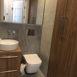 Gracz development sp zoo - Nowoczesna łazienka z umywalką nablatową na drewnianej szafce, podwieszaną toaletą i szarą płytką imitującą kamień.