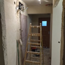 E .L .E .S . Instalacje elektryczne - Korytarz w trakcie remontu: widoczne przewody elektryczne, drabina i ślady prac budowlanych na ścianach. Etap przygotowawczy przed malowaniem.