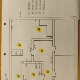 Ręcznie rysowany schemat instalacji elektrycznej mieszkania na papierze w kratkę, z zaznaczonymi punktami oświetleniowymi i gniazdami. Widoczny plan z opisami pomieszczeń.
