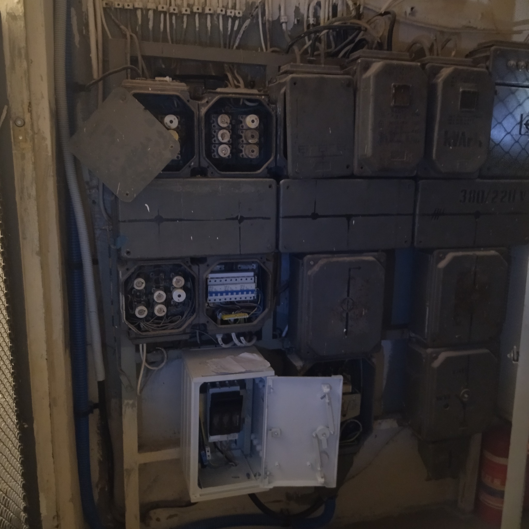 Rozdzielnica elektryczna z otwartymi skrzynkami, widoczne bezpieczniki i okablowanie. Starszy typ instalacji, szare obudowy, elementy zabezpieczeń.