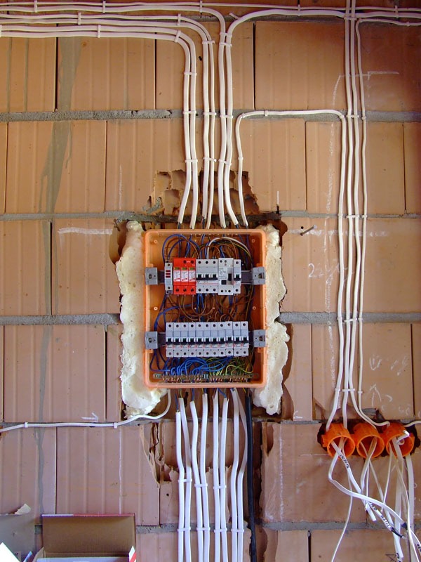 Rozdzielnica elektryczna w trakcie montażu w Głogowie. Widoczne przewody i zabezpieczenia na tle ceglanej ściany. Instalacja w trakcie prac, pianka montażowa.