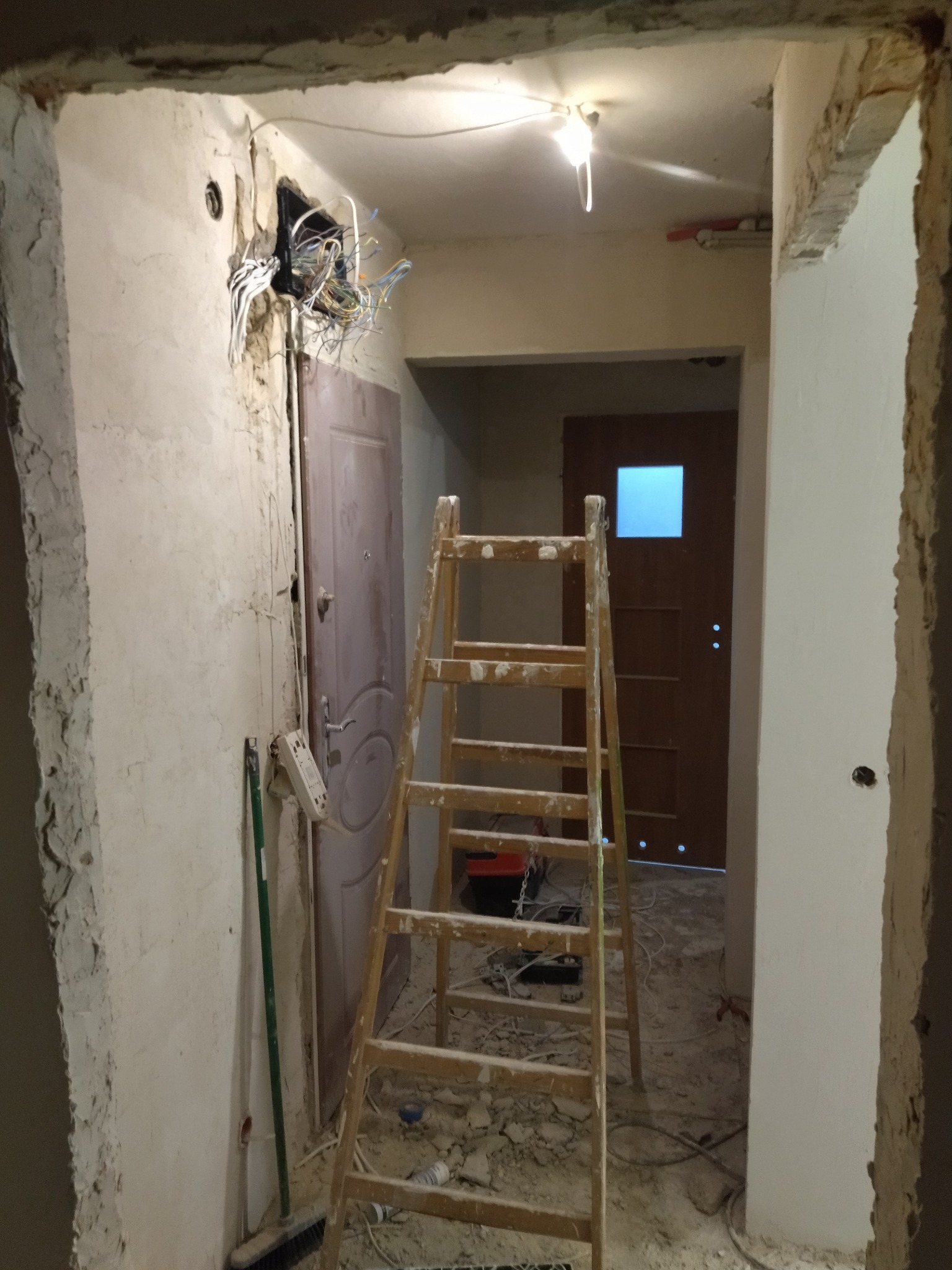 Korytarz w trakcie remontu: widoczne przewody elektryczne, drabina i ślady prac budowlanych na ścianach. Etap przygotowawczy przed malowaniem.