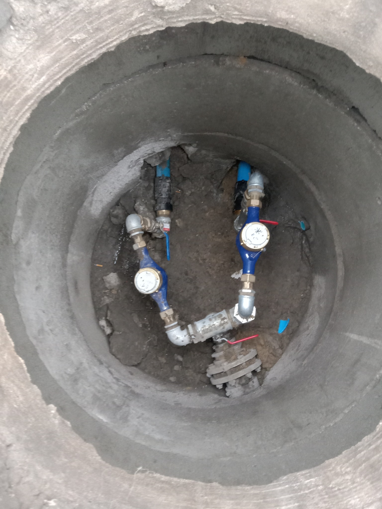 Wnętrze betonowej studzienki kanalizacyjnej z zamontowanymi wodomierzami i zaworami, widok z góry.