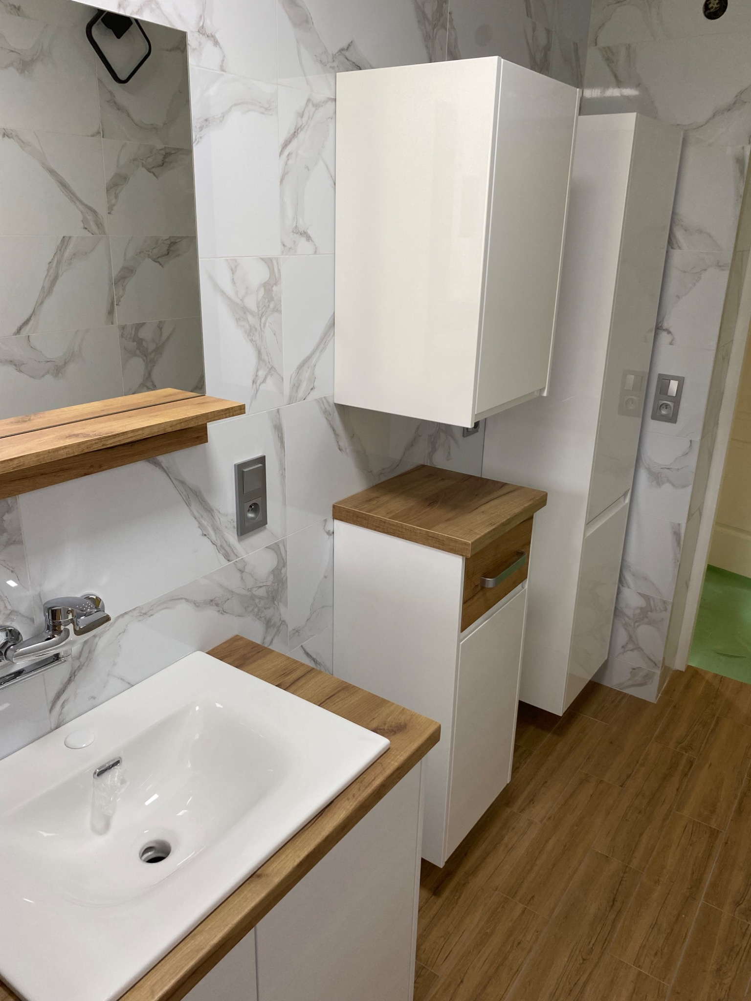 Nowoczesna łazienka z białymi szafkami z drewnianymi blatami, białą umywalką i marmurowymi płytkami na ścianach.