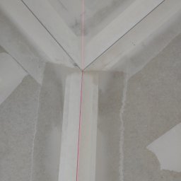 Regimex licencjonowany wykonawca firmy RIGIPS Polska. - Kąt sufitu i ściany w trakcie prac wykończeniowych, widoczna laserowa linia wyznaczająca poziom, ślady szpachli i łączenia płyt.