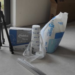 Regimex licencjonowany wykonawca firmy RIGIPS Polska. - Przygotowanie do prac wykończeniowych: torba z gipsem szpachlowym, rolki taśmy, profil aluminiowy, pudełko płyty Habito Flex, radio budowlane Makita i statyw na podłodze w surowym wnętrzu.